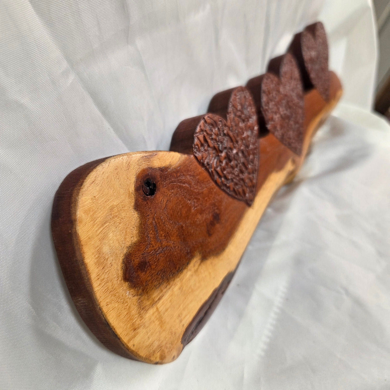 A rustic wooden decorative plaque featuring three hand carved hearts made from a single mesquite slab