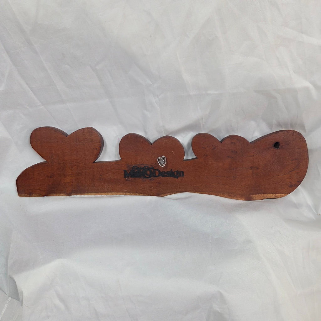 A rustic wooden decorative plaque featuring three hand carved hearts made from a single mesquite slab showing the back with the hanger and CCMD brand