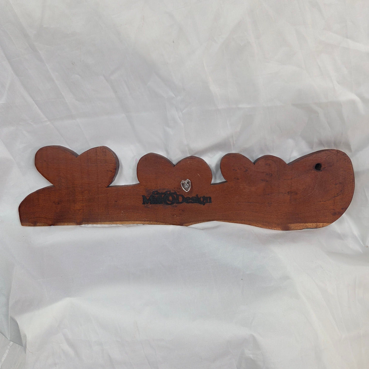A rustic wooden decorative plaque featuring three hand carved hearts made from a single mesquite slab showing the back with the hanger and CCMD brand