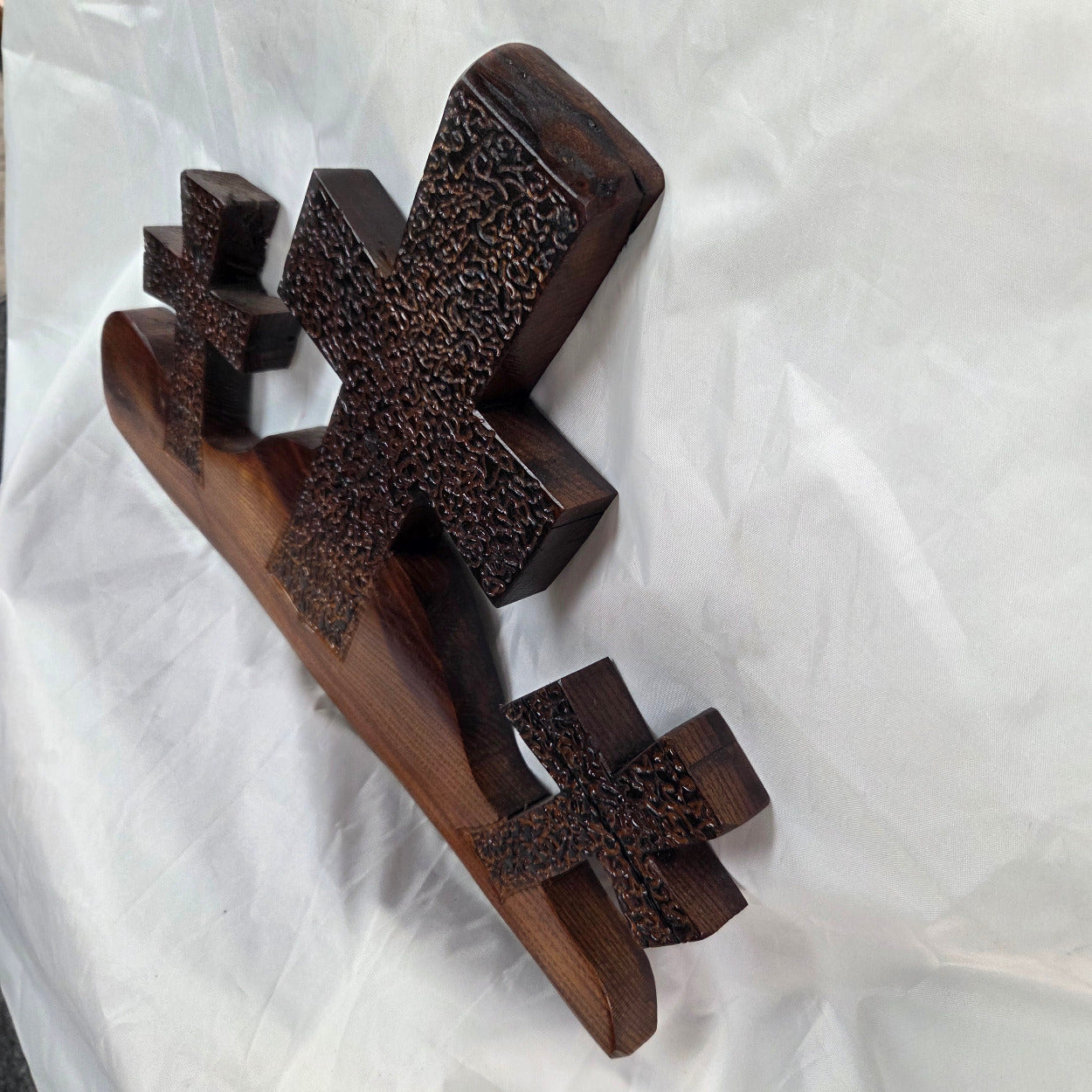 A Bois D'Arc decorative wall plaque featuring three stylized Christian crosses cut from a single slab, hand carved with burned finish sho sugi ban with natural grain 