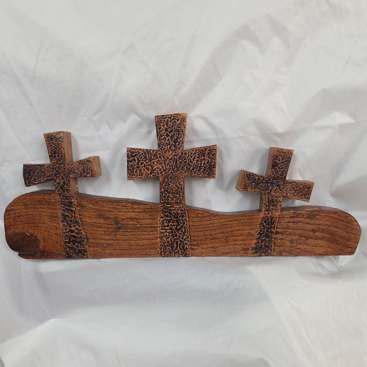 A white oak decorative wall plaque featuring three stylized Christian crosses cut from a single slab, hand carved with burned finish sho sugi ban with natural grain 