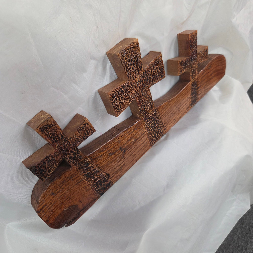 A white oak decorative wall plaque featuring three stylized Christian crosses cut from a single slab, hand carved with burned finish sho sugi ban with natural grain 