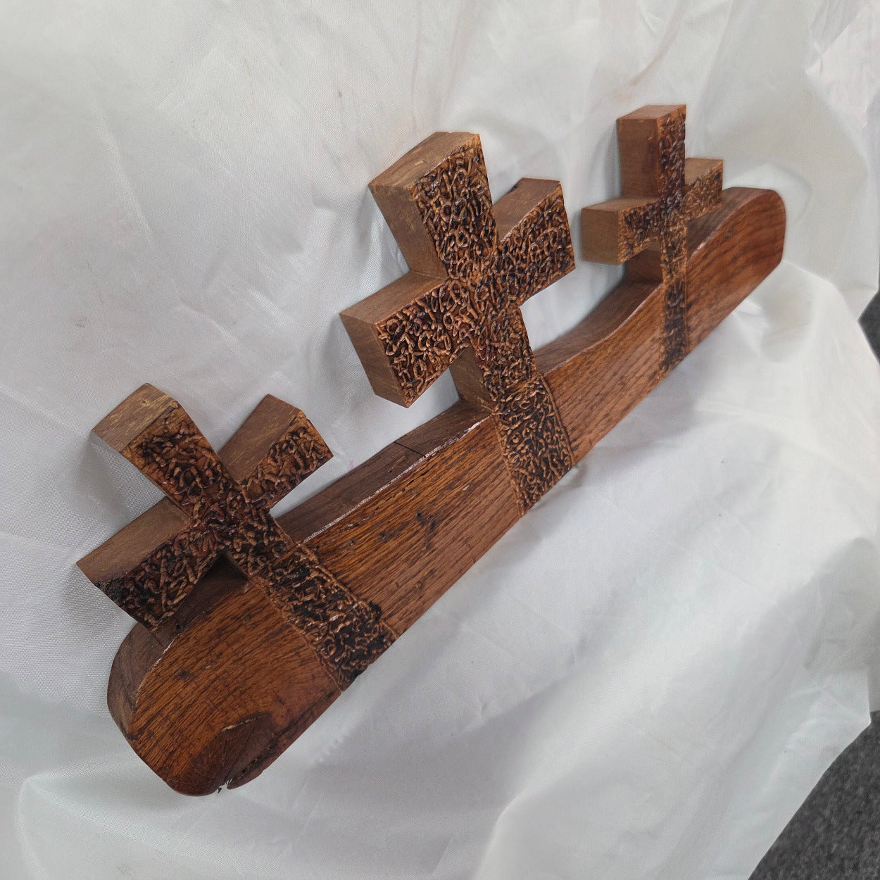 A white oak decorative wall plaque featuring three stylized Christian crosses cut from a single slab, hand carved with burned finish sho sugi ban with natural grain 