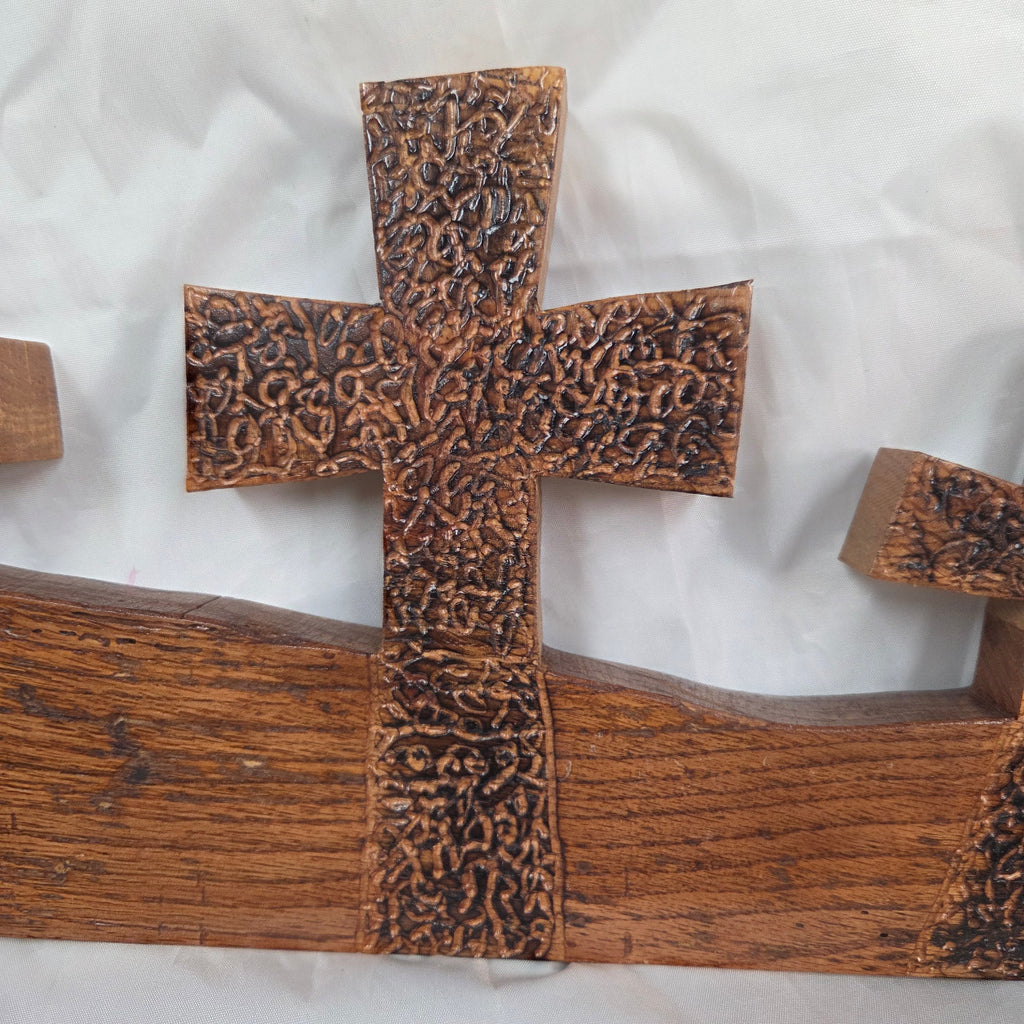 A white oak decorative wall plaque featuring three stylized Christian crosses cut from a single slab, hand carved with burned finish sho sugi ban with natural grain 