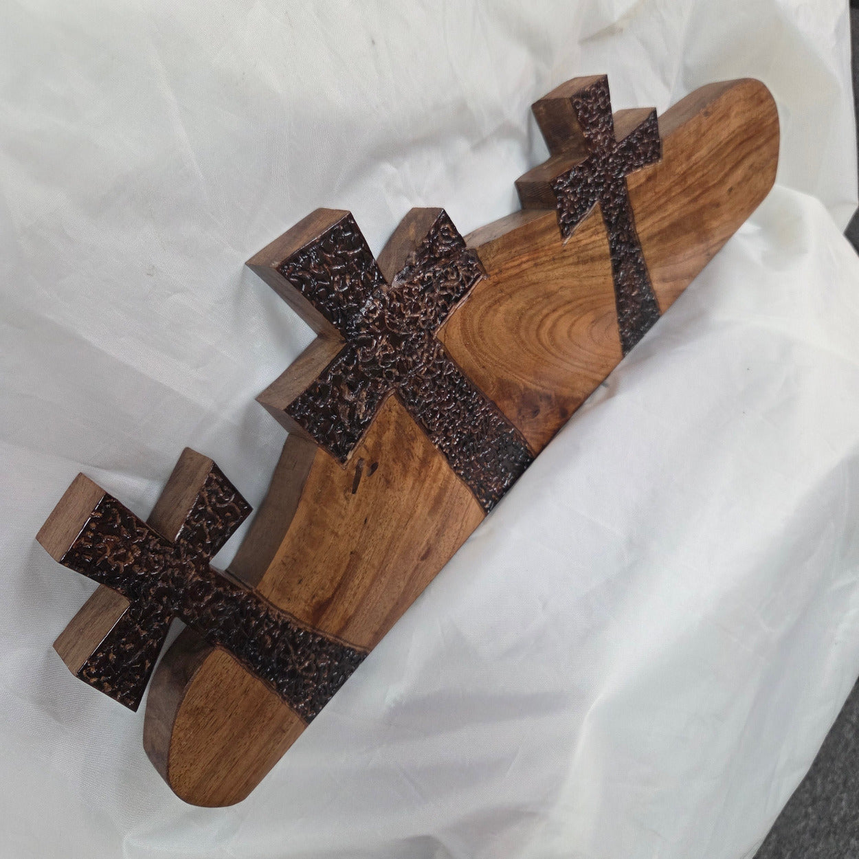 A Pecan decorative wall plaque featuring three stylized Christian crosses cut from a single slab, hand carved with burned finish sho sugi ban with natural grain 