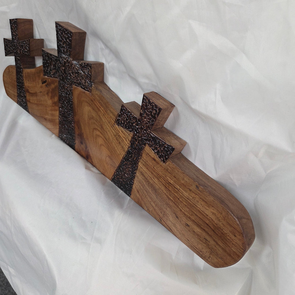 A Pecan decorative wall plaque featuring three stylized Christian crosses cut from a single slab, hand carved with burned finish sho sugi ban with natural grain 
