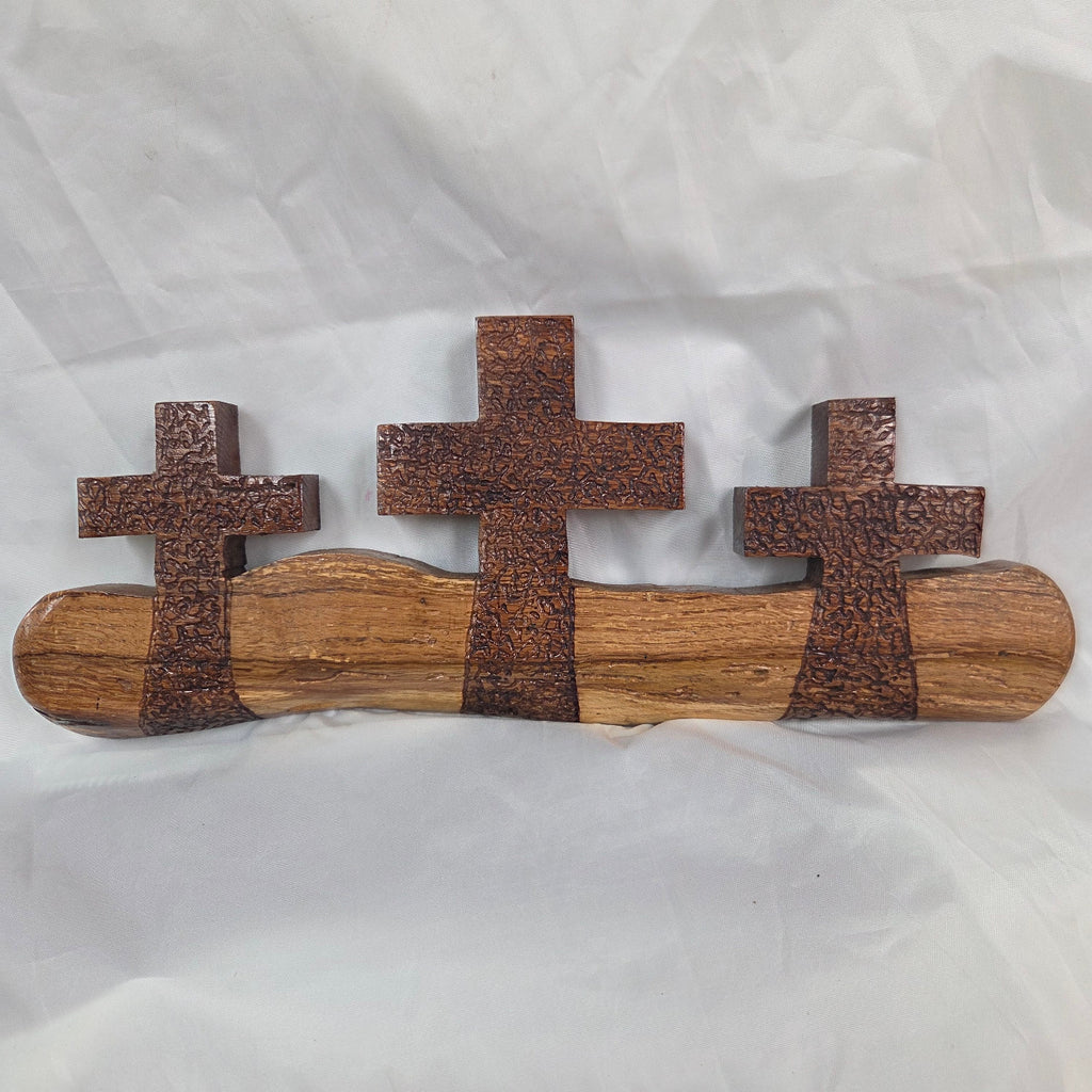 A white oak decorative wall plaque featuring three stylized Christian crosses cut from a single slab, hand carved with dark brown stained crosses and natural color base
