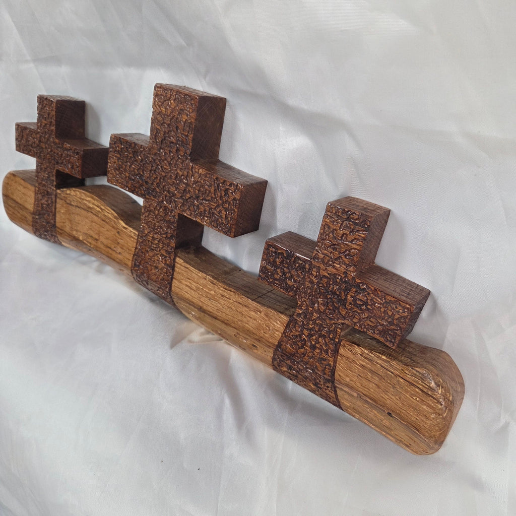 A white oak decorative wall plaque featuring three stylized Christian crosses cut from a single slab, hand carved with dark brown stained crosses and natural color base