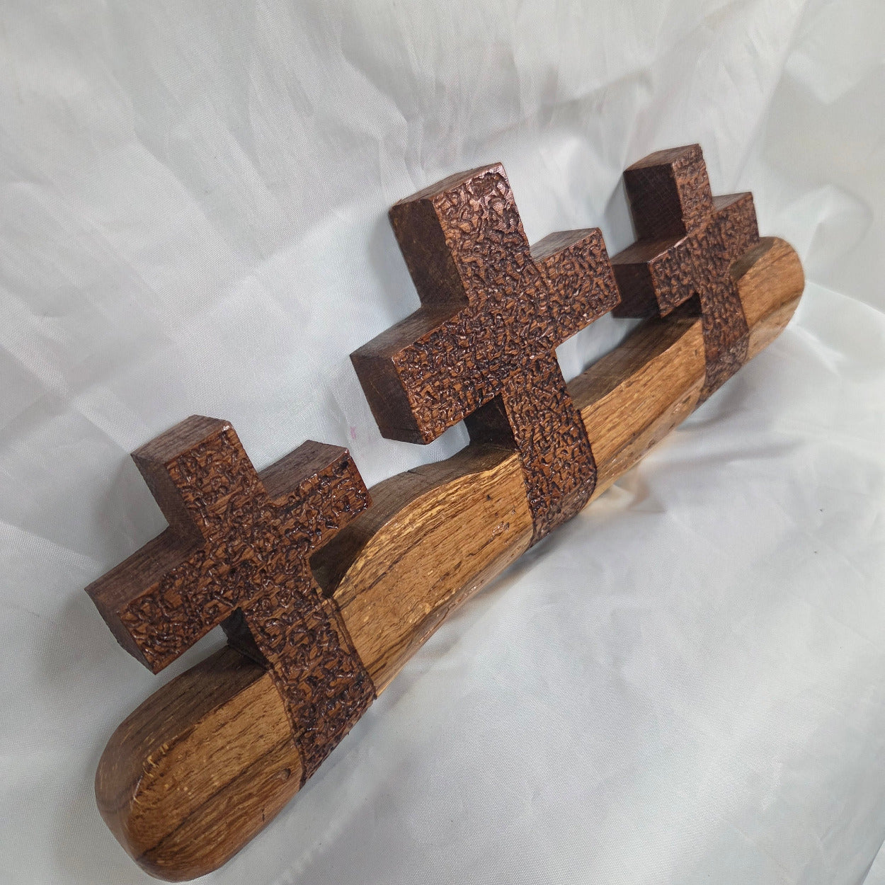 A white oak decorative wall plaque featuring three stylized Christian crosses cut from a single slab, hand carved with dark brown stained crosses and natural color base