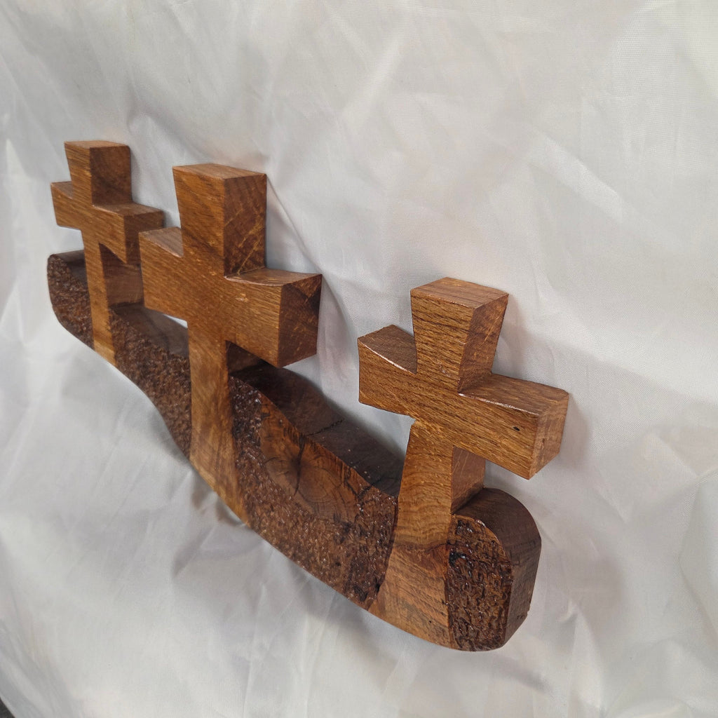 A white oak decorative wall plaque featuring three stylized Christian crosses cut from a single slab, hand carved with dark brown wooden base, 