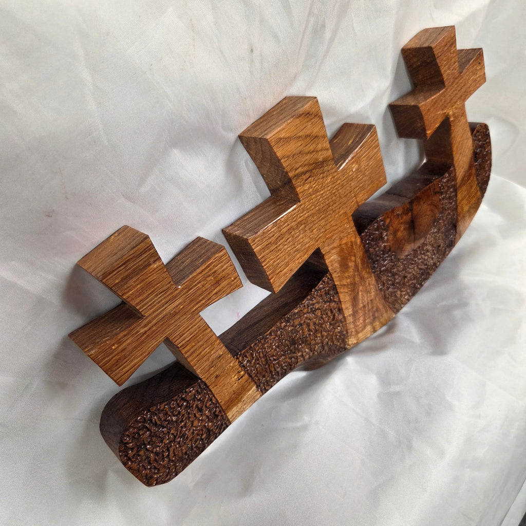 A white oak decorative wall plaque featuring three stylized Christian crosses cut from a single slab, hand carved with dark brown wooden base, 