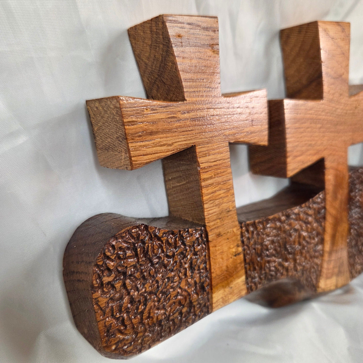 A white oak decorative wall plaque featuring three stylized Christian crosses cut from a single slab, hand carved with dark brown wooden base, 