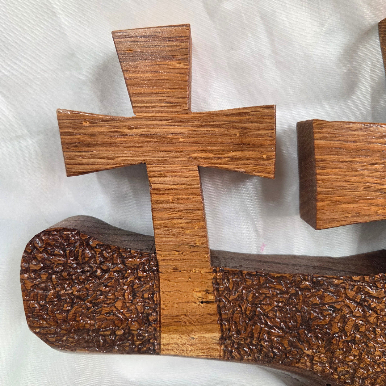 A white oak decorative wall plaque featuring three stylized Christian crosses cut from a single slab, hand carved with dark brown wooden base, 