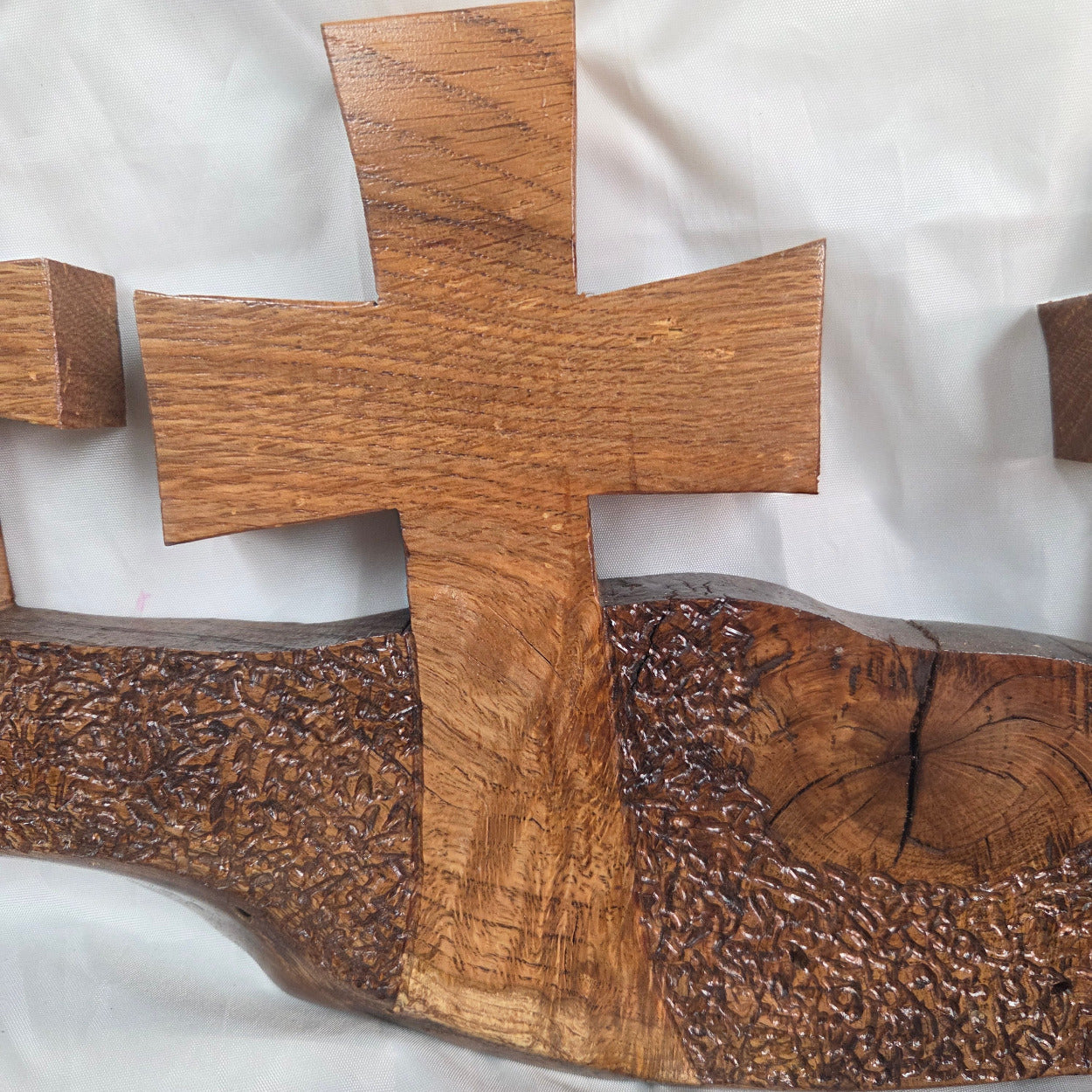 A white oak decorative wall plaque featuring three stylized Christian crosses cut from a single slab, hand carved with dark brown wooden base, 