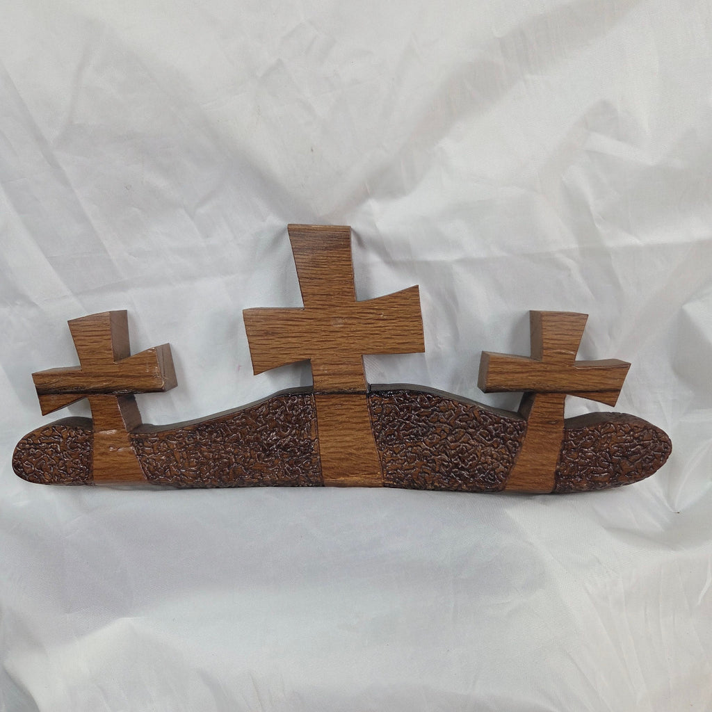 A white oak decorative wall plaque featuring three stylized Christian crosses cut from a single slab, hand carved with dark brown wooden base, 
