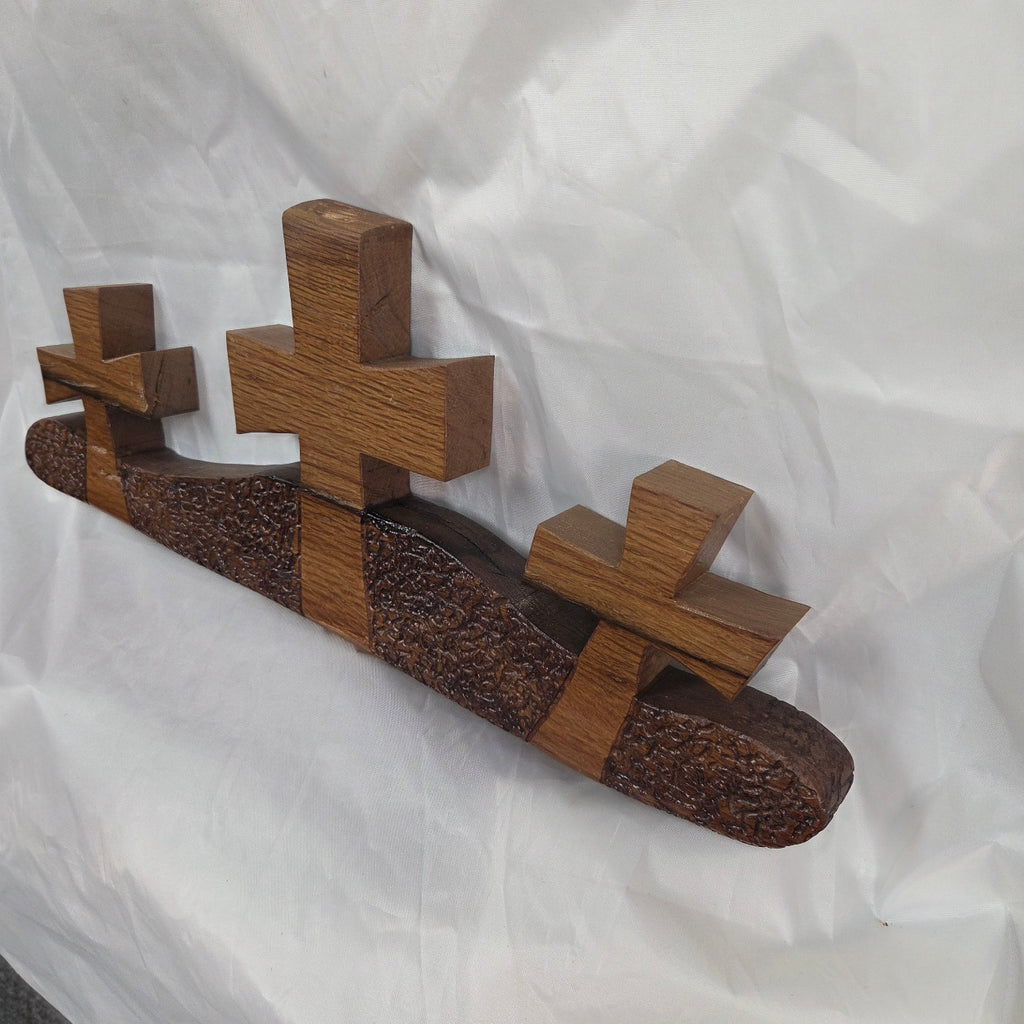 A white oak decorative wall plaque featuring three stylized Christian crosses cut from a single slab, hand carved with dark brown wooden base, 