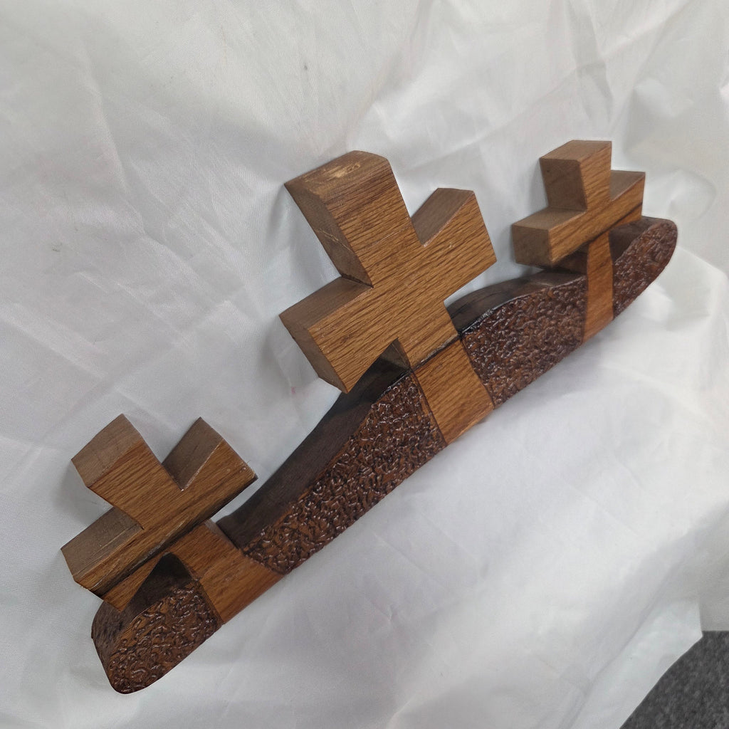 A white oak decorative wall plaque featuring three stylized Christian crosses cut from a single slab, hand carved with dark brown wooden base, 