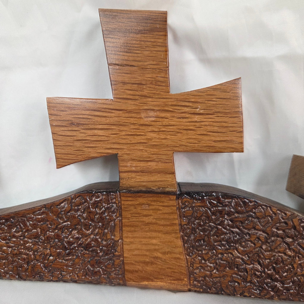 A white oak decorative wall plaque featuring three stylized Christian crosses cut from a single slab, hand carved with dark brown wooden base, 
