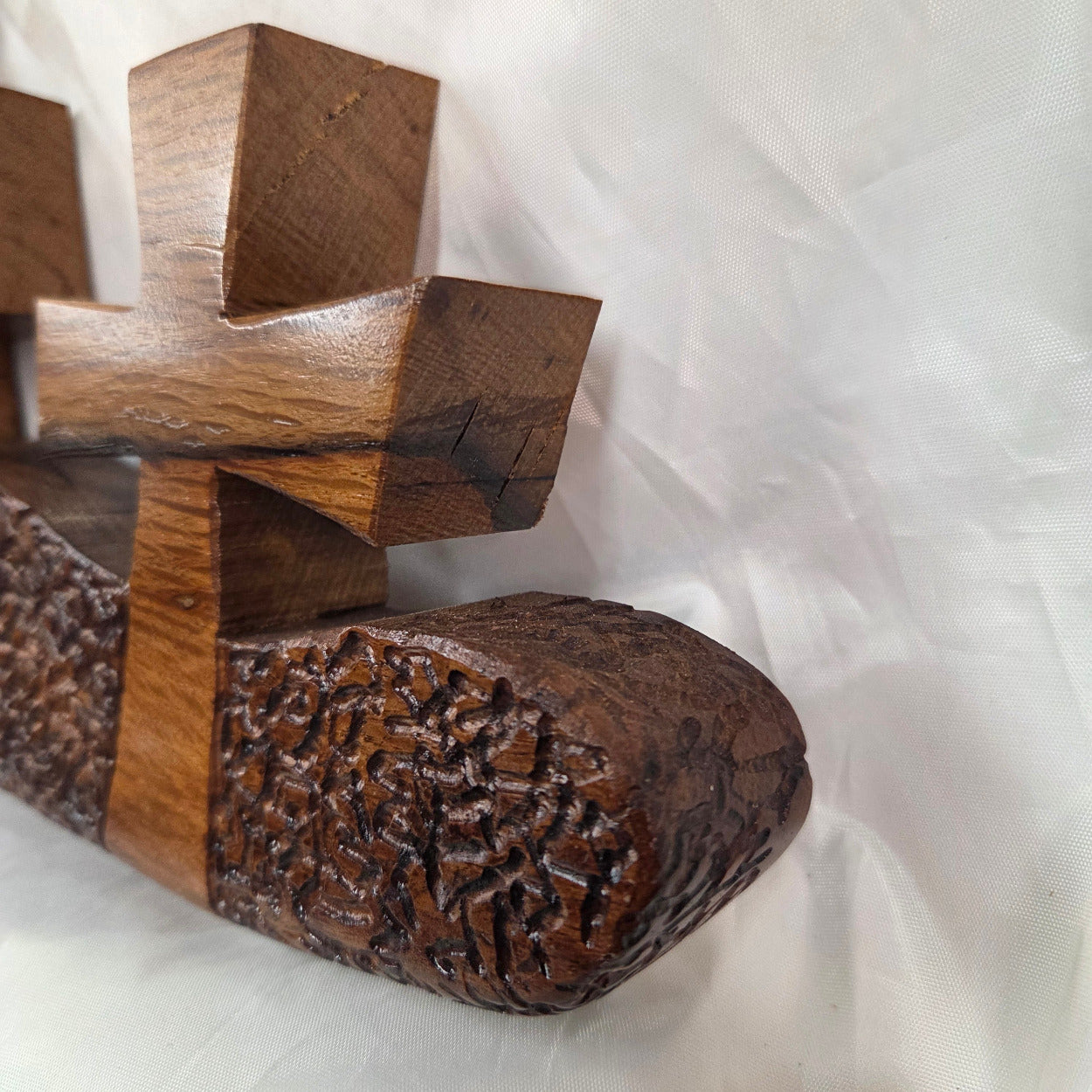 A white oak decorative wall plaque featuring three stylized Christian crosses cut from a single slab, hand carved with dark brown wooden base, 