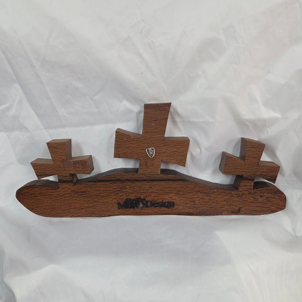 A white oak decorative wall plaque featuring three stylized Christian crosses cut from a single slab, hand carved with dark brown wooden base, 