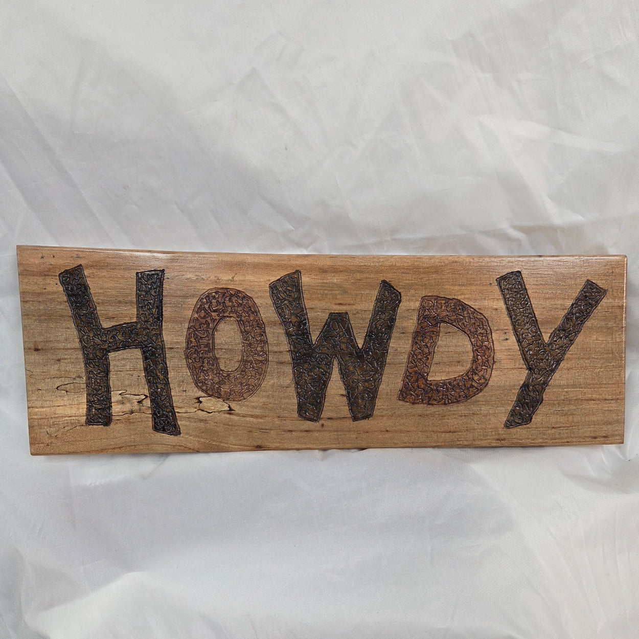 A rustic rectangular pecan sign with the word 'HOWDY' hand carved in dark brown burnt lettering,