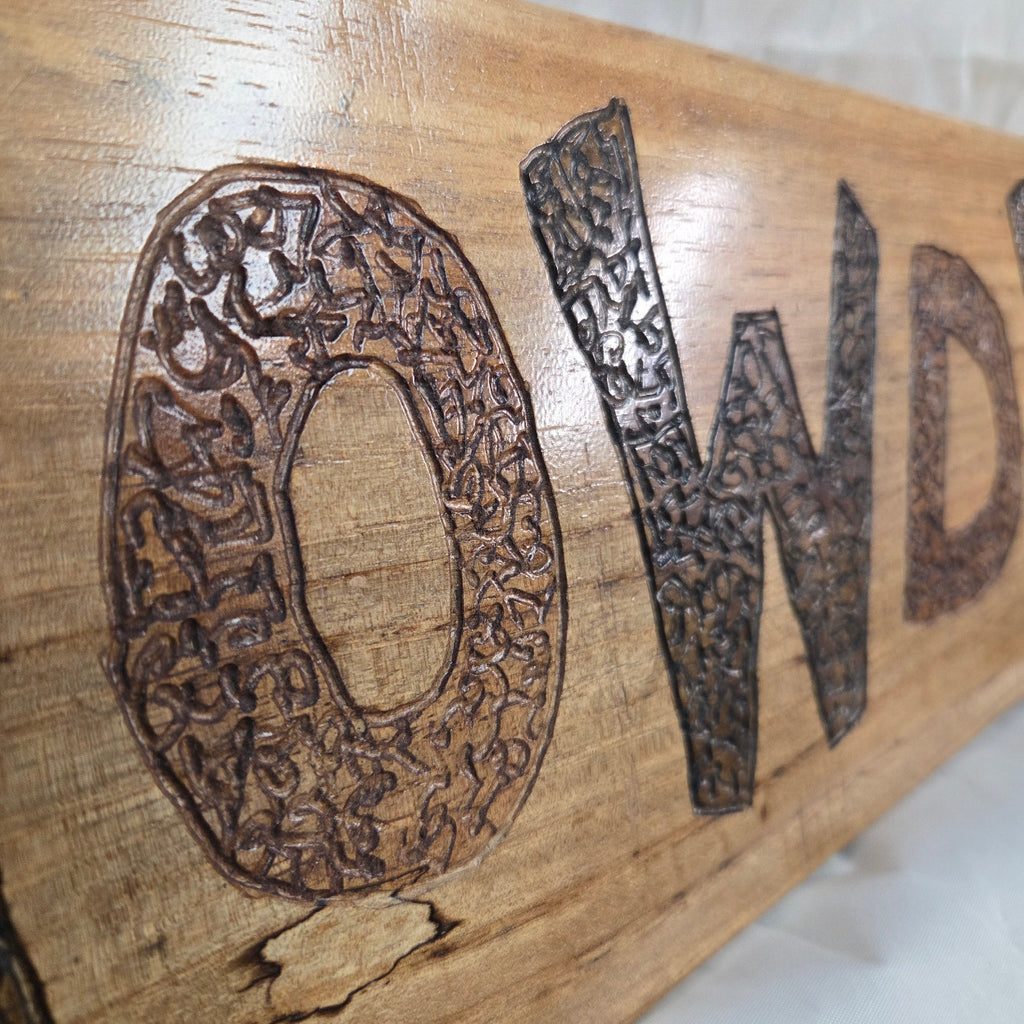 A rustic rectangular pecan sign with the word 'HOWDY' hand carved in dark brown burnt lettering,