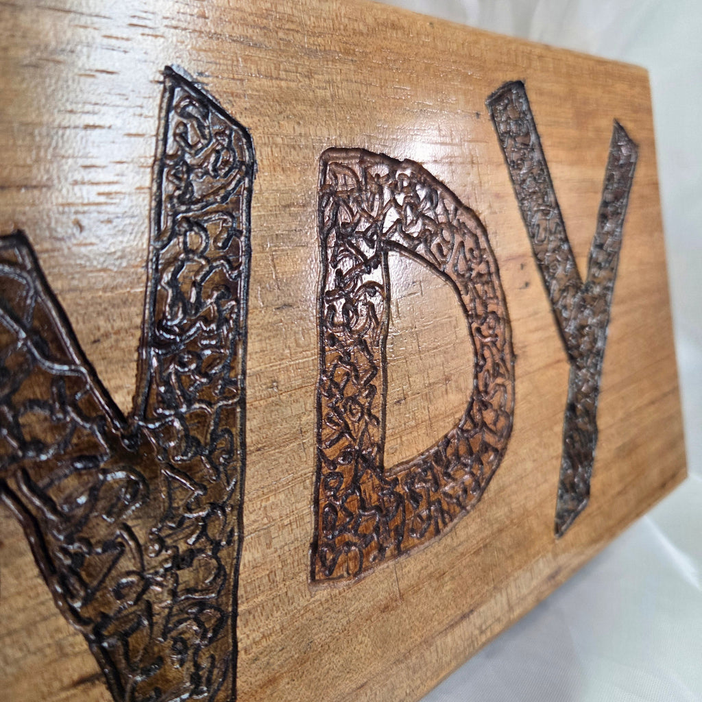 A rustic rectangular pecan sign with the word 'HOWDY' hand carved in dark brown burnt lettering,