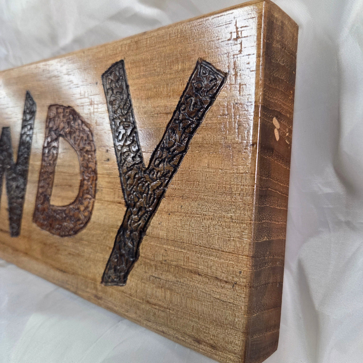 A rustic rectangular pecan sign with the word 'HOWDY' hand carved in dark brown burnt lettering,