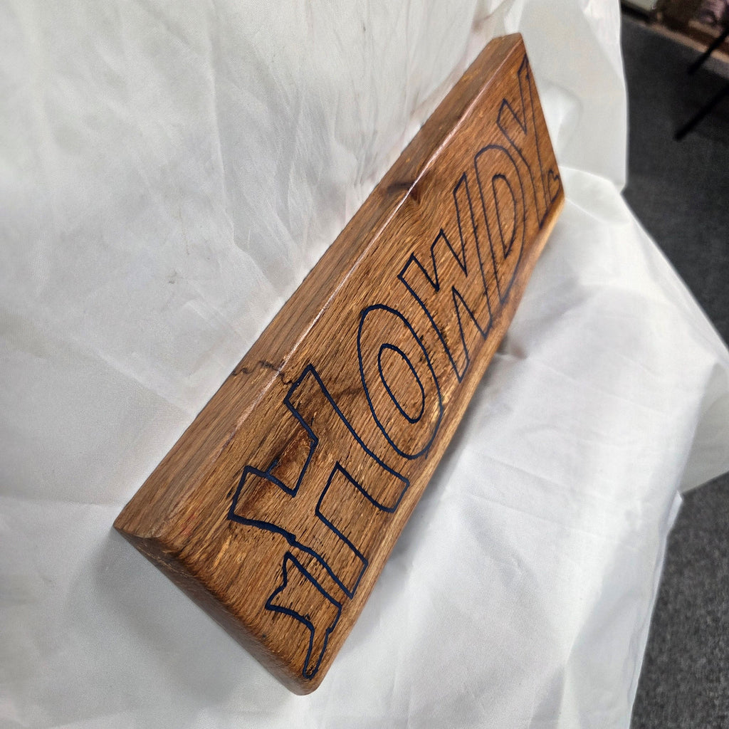 A rectangular white oak sign with a natural brown wood grain finish, featuring the word 'HOWDY' cut out in blue epoxy outline lettering, 
