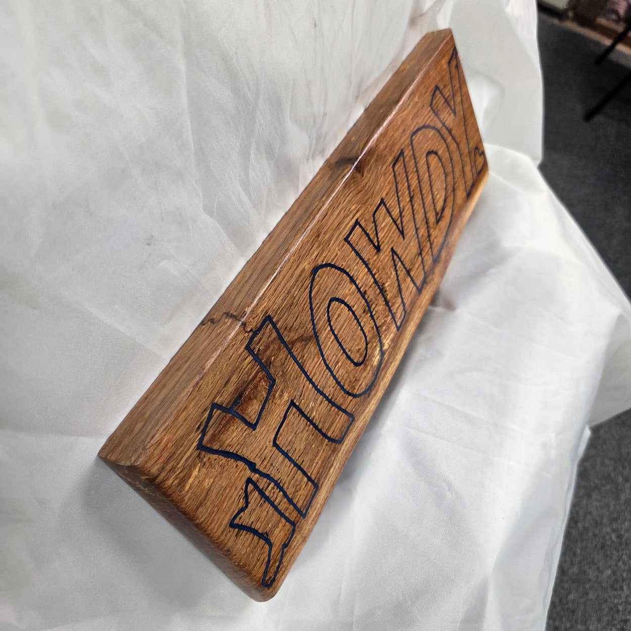 A rectangular white oak sign with a natural brown wood grain finish, featuring the word 'HOWDY' cut out in blue epoxy outline lettering, 