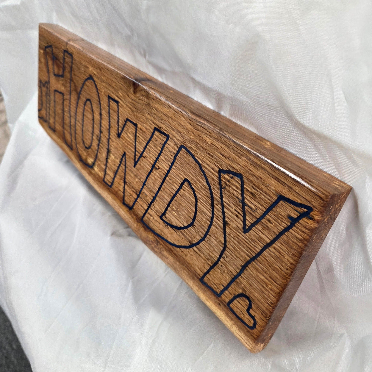 A rectangular white oak sign with a natural brown wood grain finish, featuring the word 'HOWDY' cut out in blue epoxy outline lettering, 