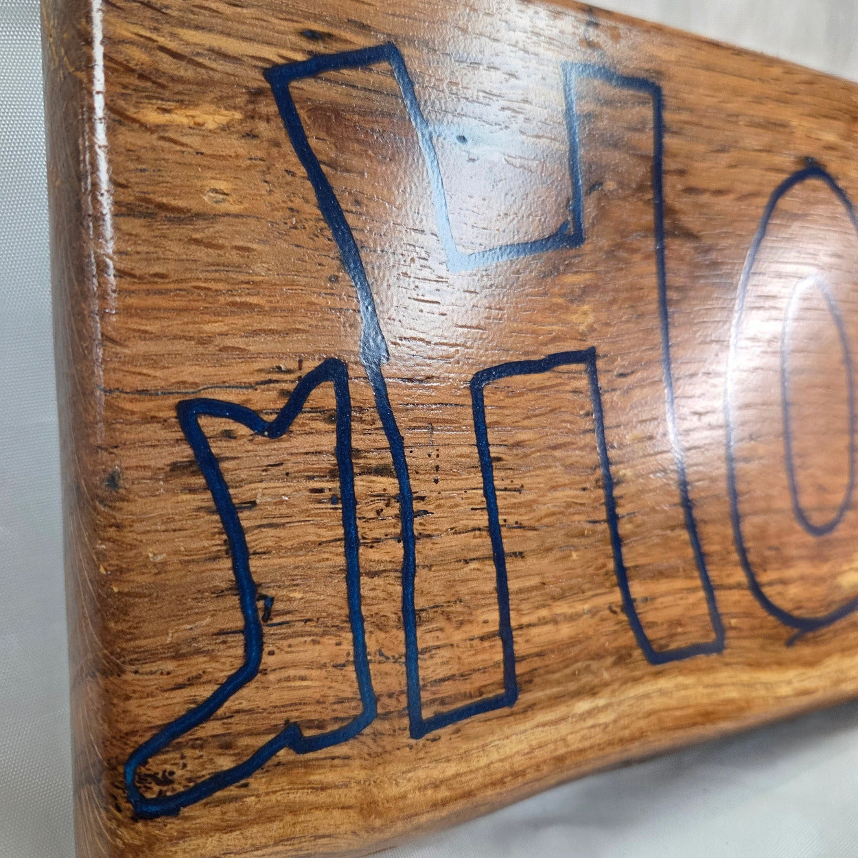 close up A rectangular white oak sign with a natural brown wood grain finish, featuring the word 'HOWDY' cut out in blue epoxy outline lettering, 