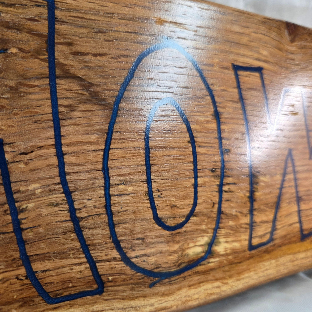 close up A rectangular white oak sign with a natural brown wood grain finish, featuring the word 'HOWDY' cut out in blue epoxy outline lettering, 