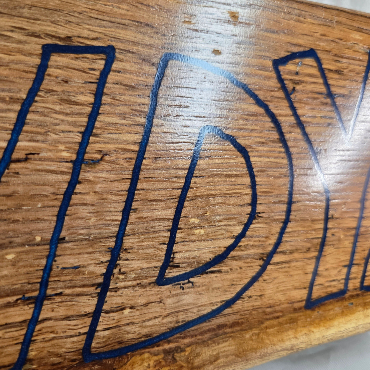 close up A rectangular white oak sign with a natural brown wood grain finish, featuring the word 'HOWDY' cut out in blue epoxy outline lettering, 