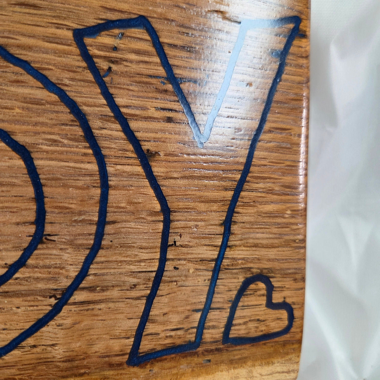 close up A rectangular white oak sign with a natural brown wood grain finish, featuring the word 'HOWDY' cut out in blue epoxy outline lettering, 