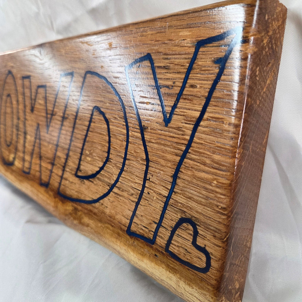 close up A rectangular white oak sign with a natural brown wood grain finish, featuring the word 'HOWDY' cut out in blue epoxy outline lettering, 