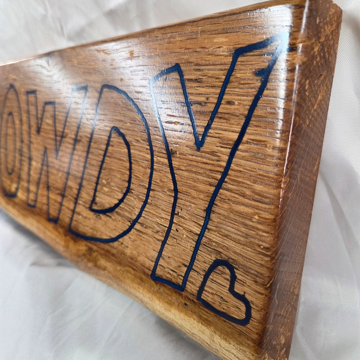 close up A rectangular white oak sign with a natural brown wood grain finish, featuring the word 'HOWDY' cut out in blue epoxy outline lettering, 
