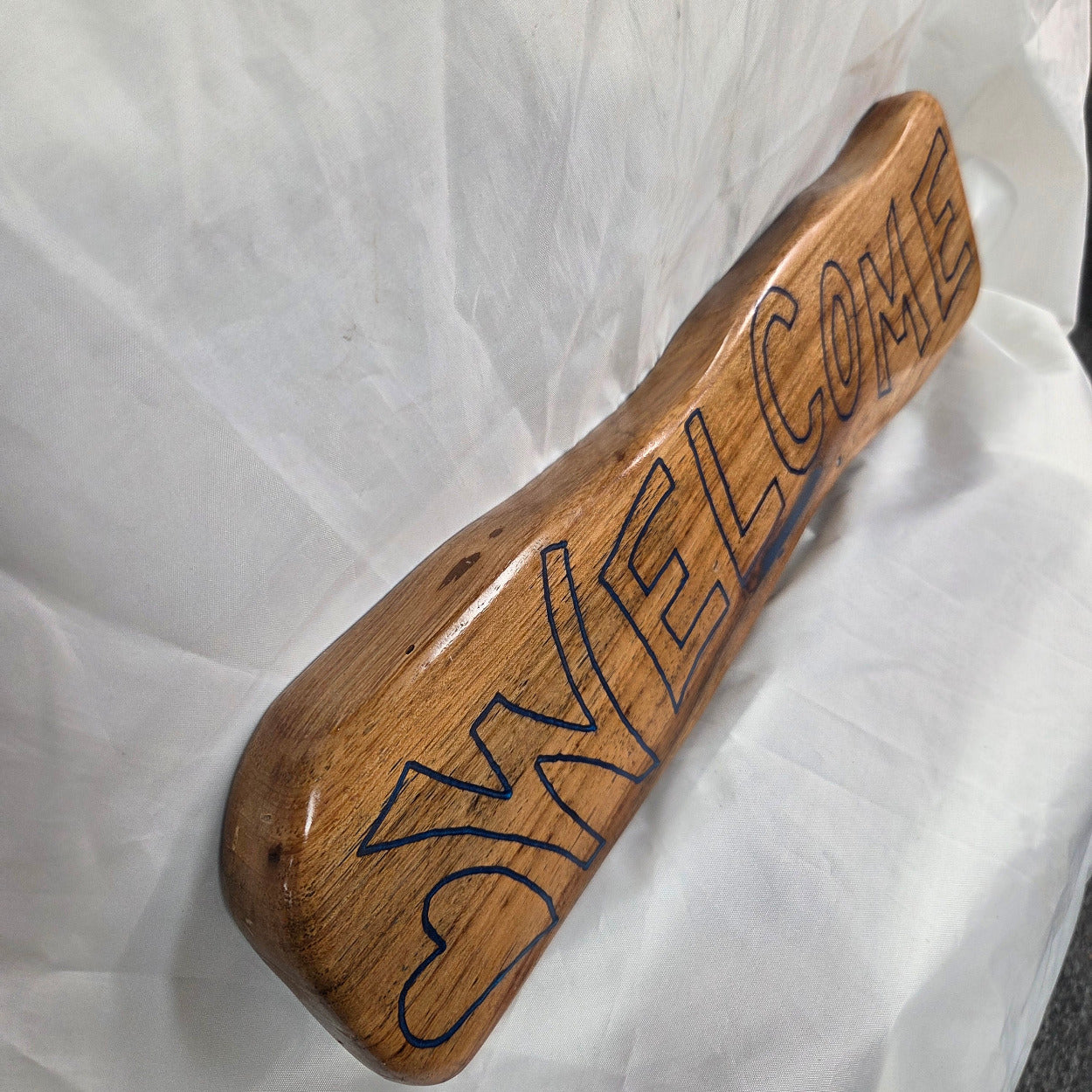 A rustic, live-edge white oak sign featuring the word 'WELCOME' in a blue epoxy outline font carved into the natural wood grain, 