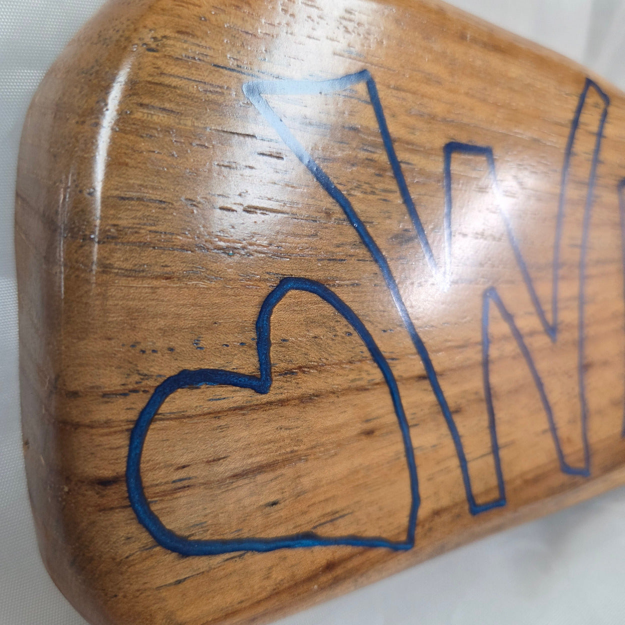close up A rustic, live-edge white oak sign featuring the word 'WELCOME' in a blue epoxy outline font carved into the natural wood grain, 
