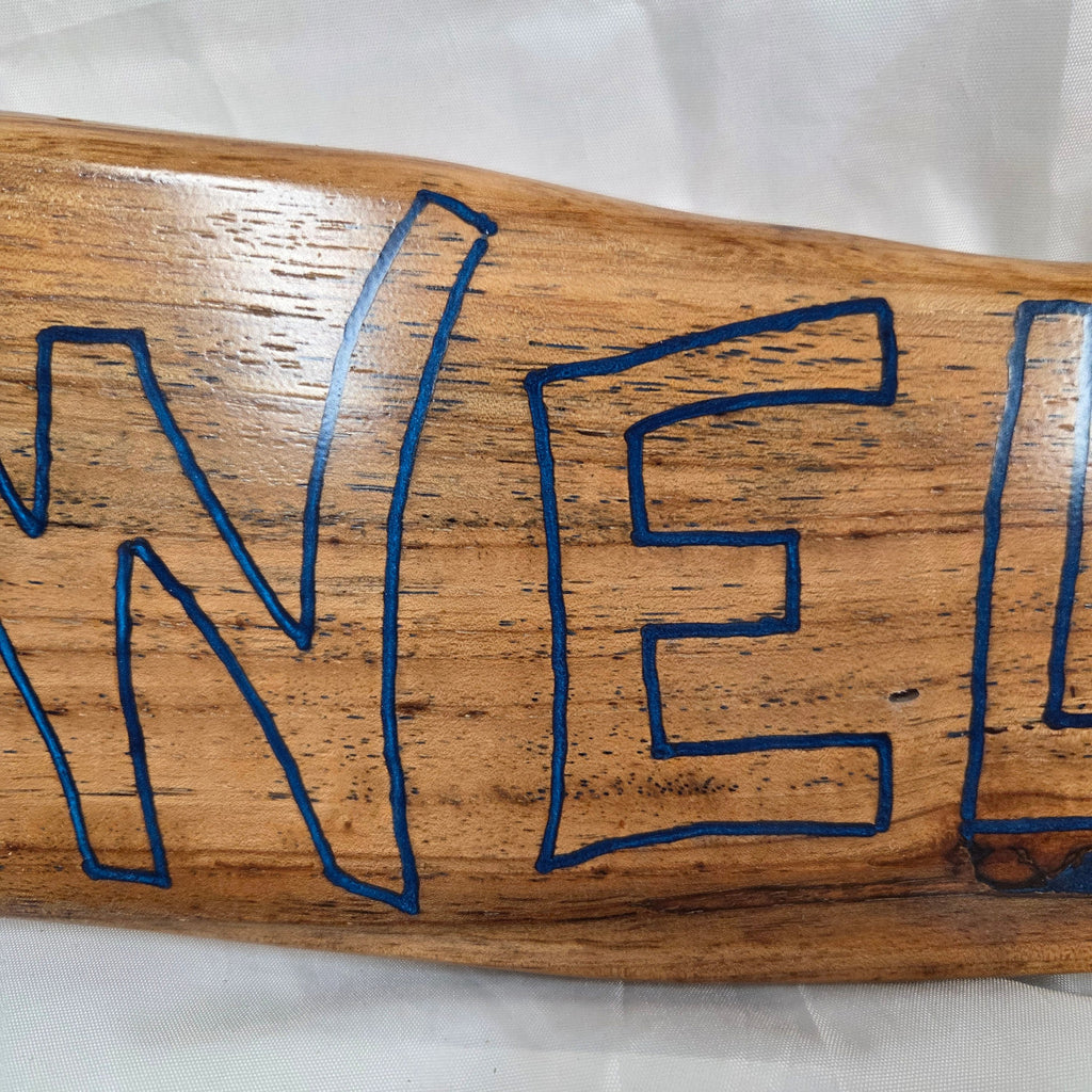 A rustic, live-edge white oak sign featuring the word 'WELCOME' in a blue epoxy outline font carved into the natural wood grain, 