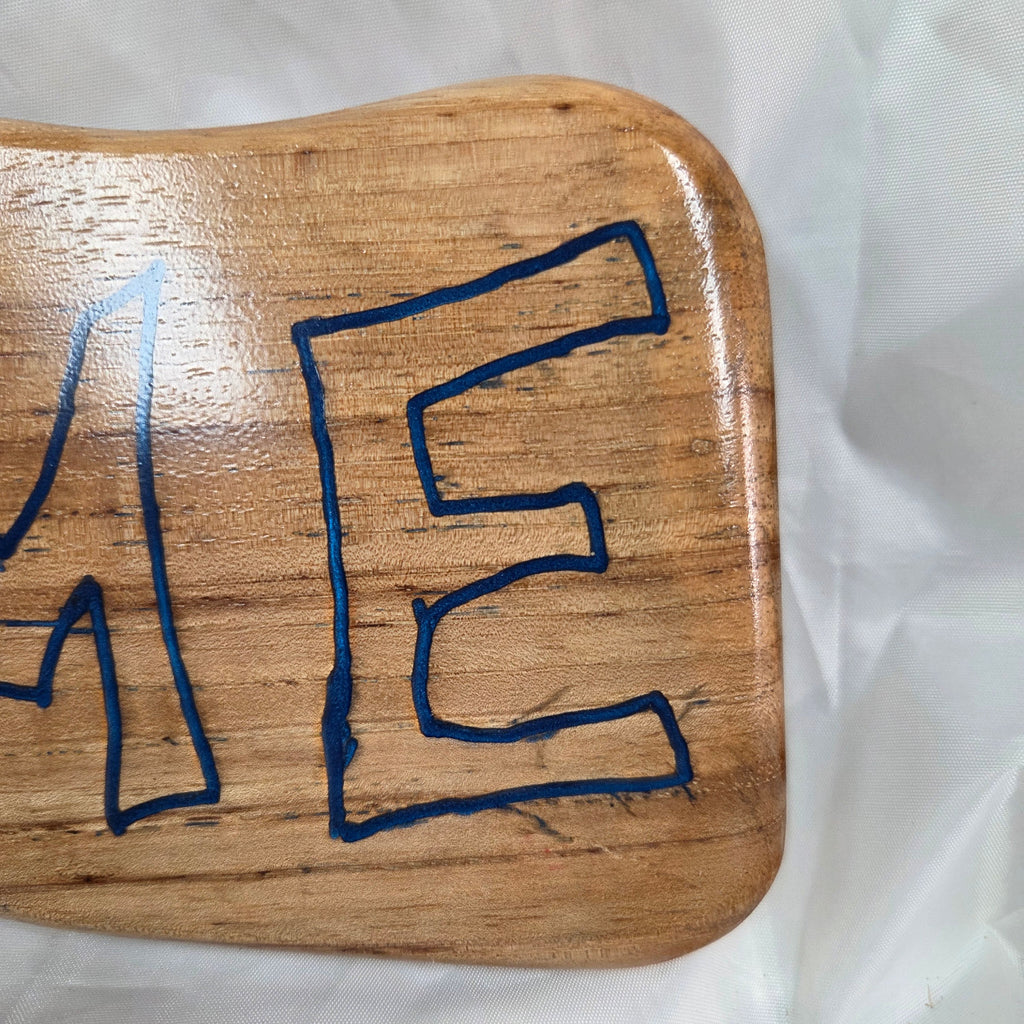 A rustic, live-edge white oak sign featuring the word 'WELCOME' in a blue epoxy outline font carved into the natural wood grain, 