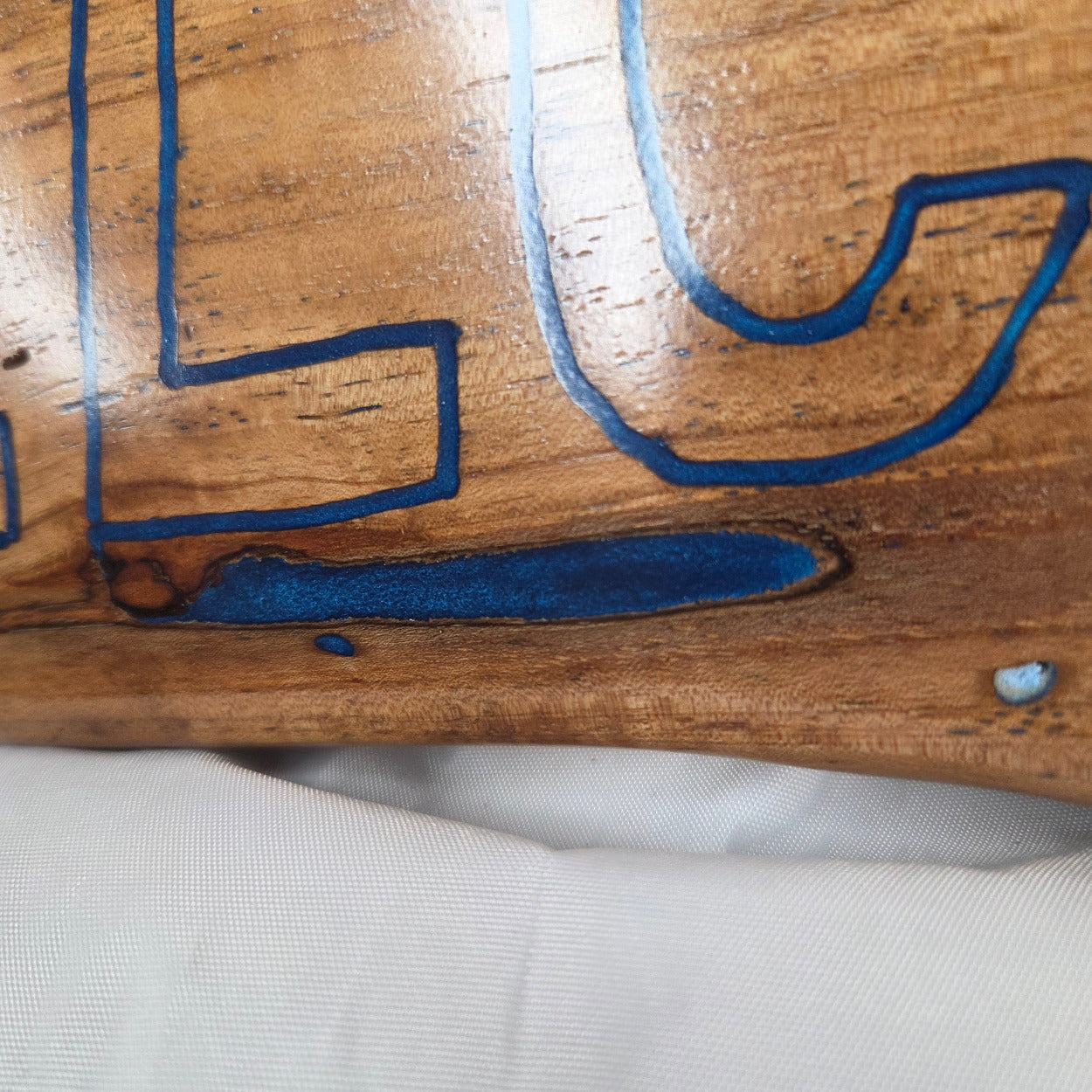 A rustic, live-edge white oak sign featuring the word 'WELCOME' in a blue epoxy outline font carved into the natural wood grain, 