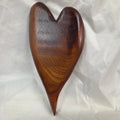 A heart-shaped mesquite wall art with a polished finish, showcasing natural wood grain, resting on a wrinkled white fabric background.