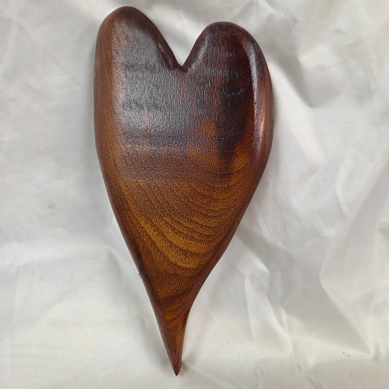 A heart-shaped mesquite wall art with a polished finish, showcasing natural wood grain, resting on a wrinkled white fabric background.