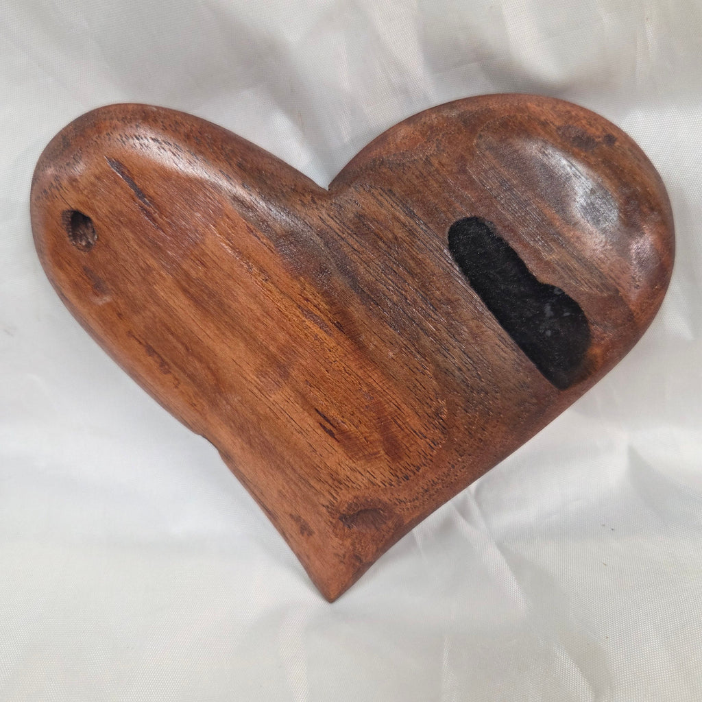 A heart-shaped wooden object with a smooth brown finish and a dark recessed slot near the top, photographed on a wrinkled white surface.