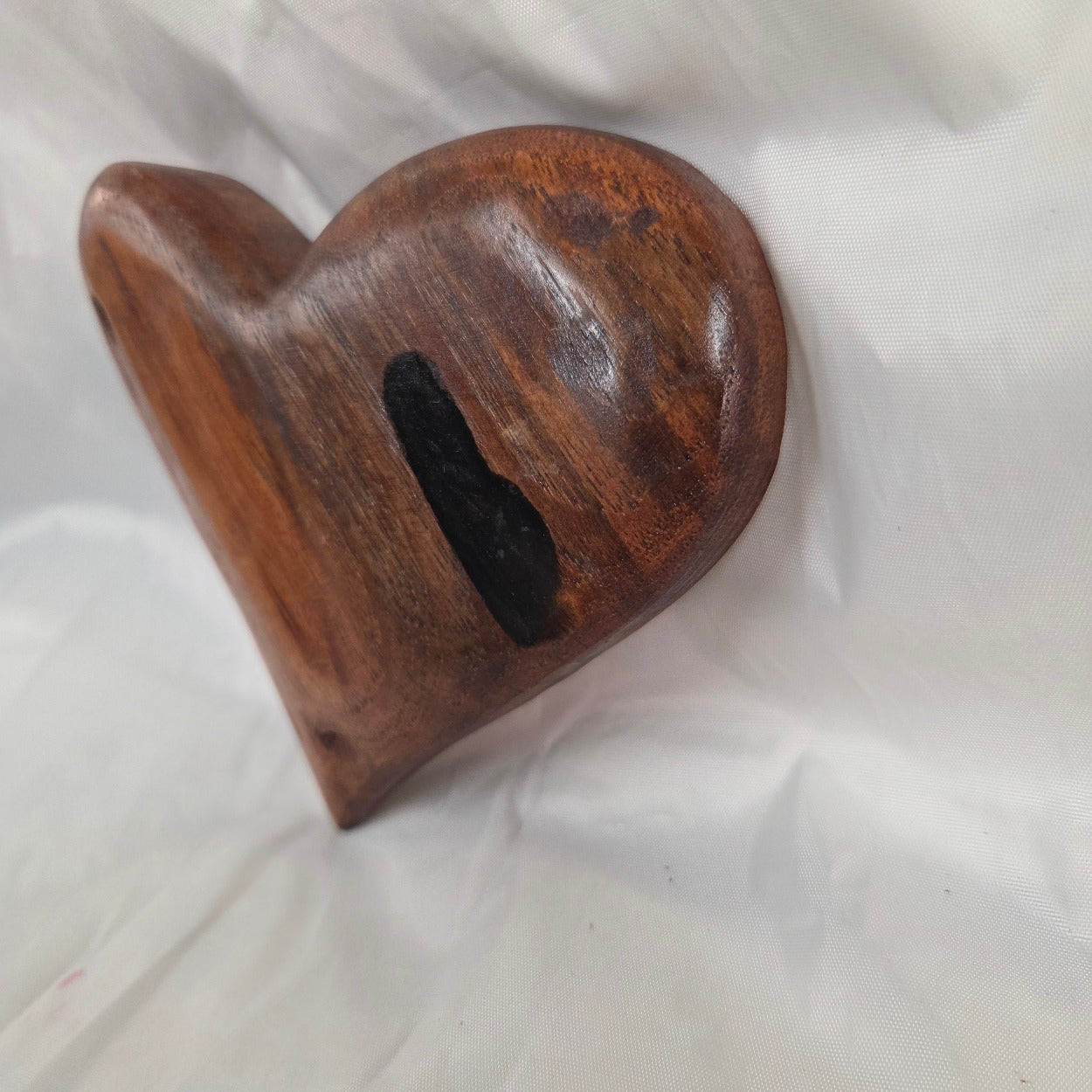 A small carved wooden hanging heart wall art with a smooth dark brown finish, photographed on wrinkled white fabric.