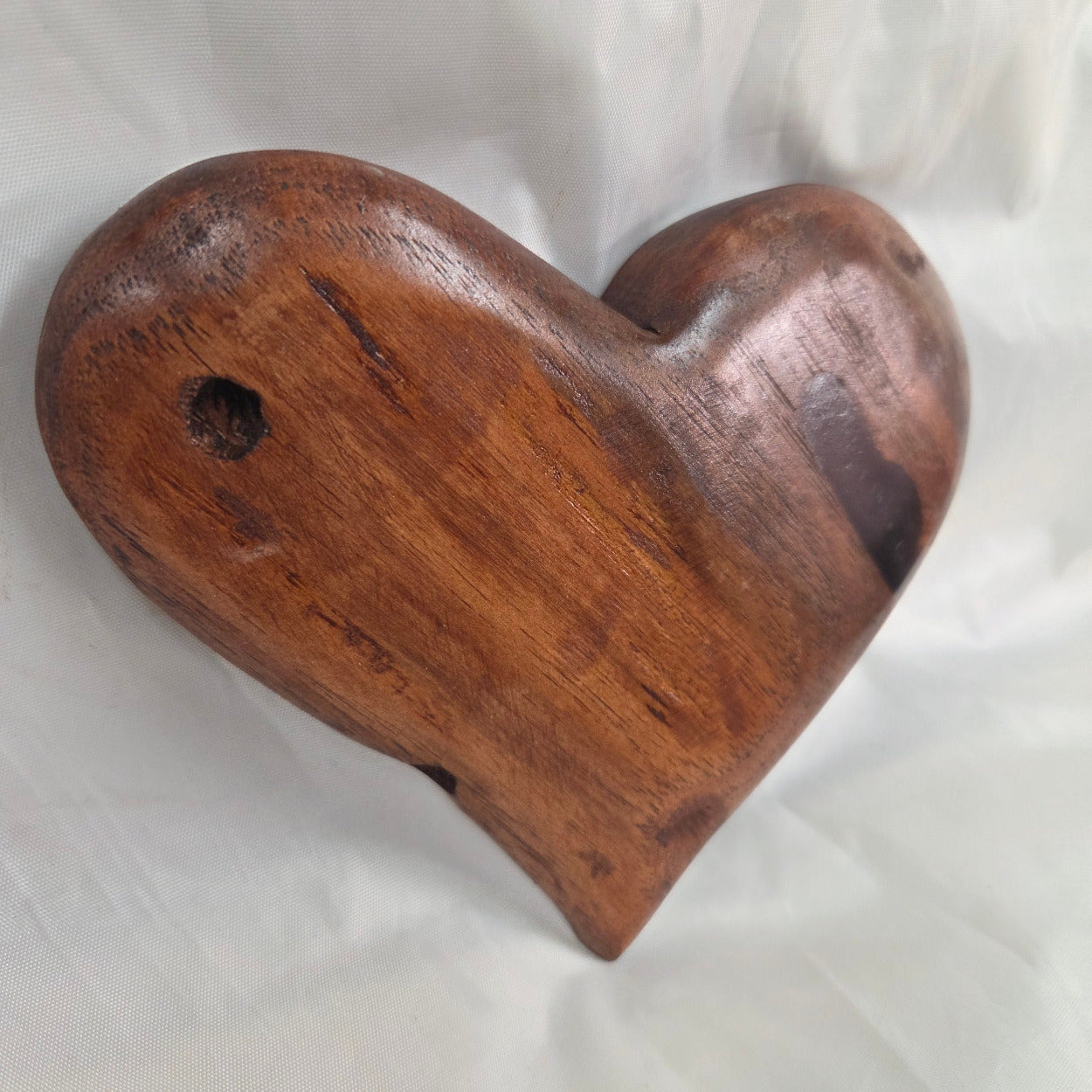 A heart-shaped wooden sculpture with a polished finish and natural grain, resting on a white fabric background.