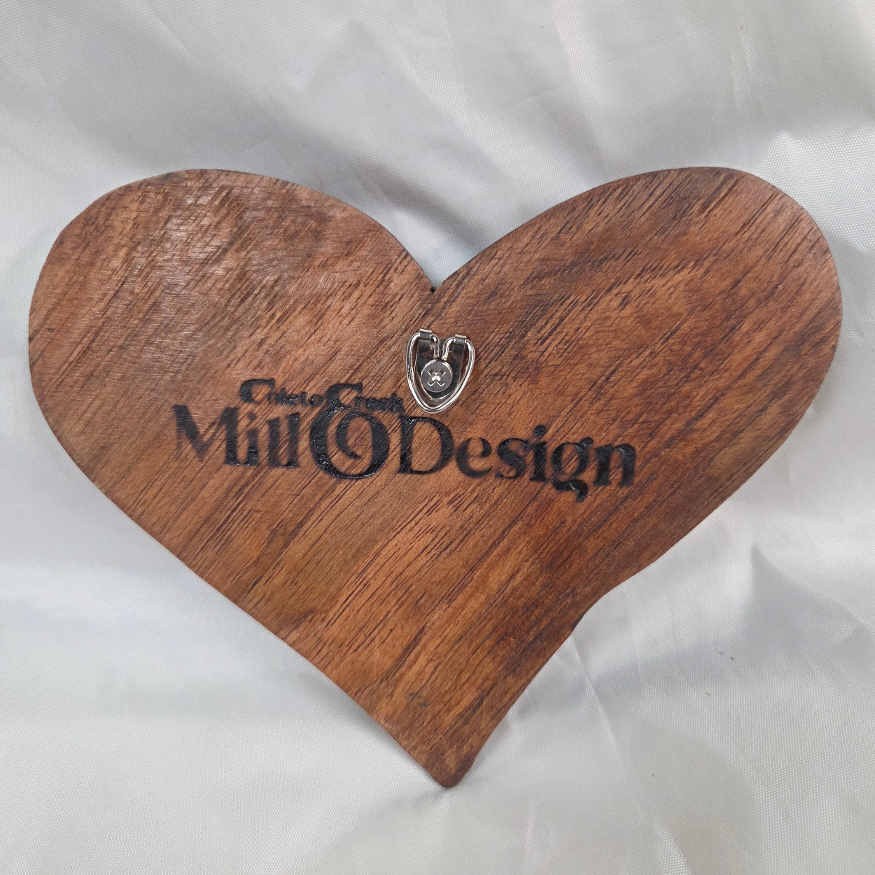 A small carved wooden hanging heart wall art with a smooth dark brown finish, photographed on wrinkled white fabric.