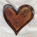 A heart-shaped wooden hanging heart with a highly textured, carved pattern on the interior, photographed on a wrinkled white fabric background.