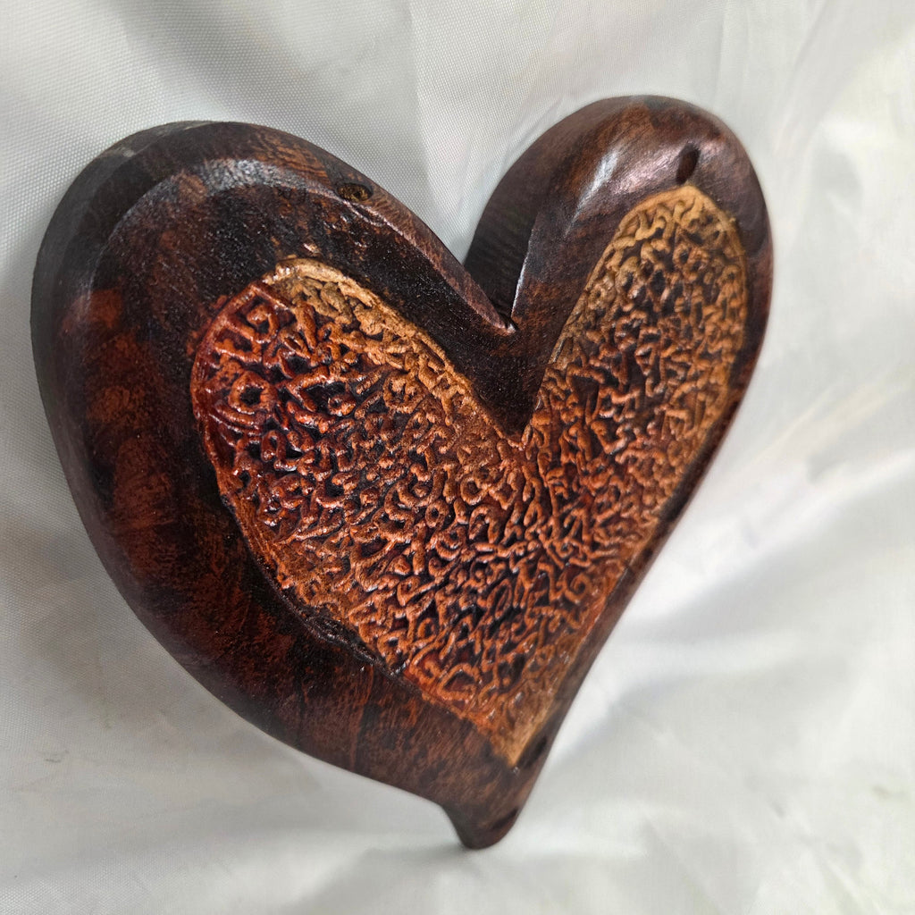 A heart-shaped wooden hanging heart with a highly textured, carved pattern on the interior, photographed on a wrinkled white fabric background.